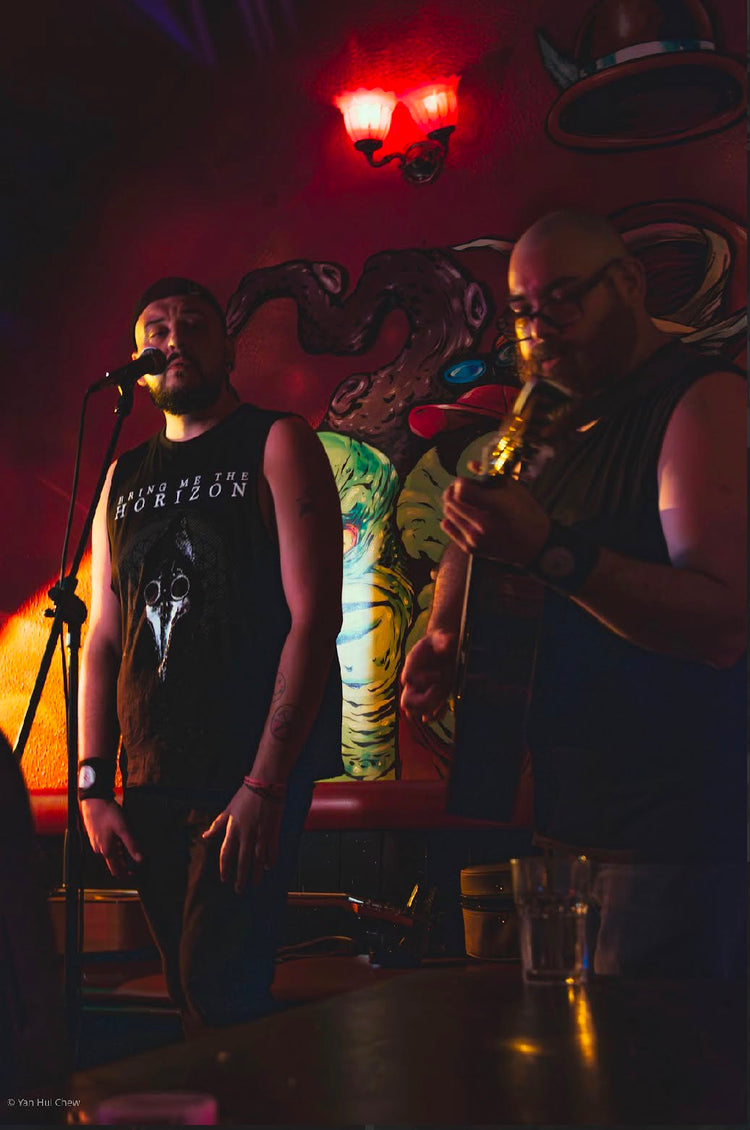 No Fixed Point performing live, one singing at the mic and one playing guitar under red light